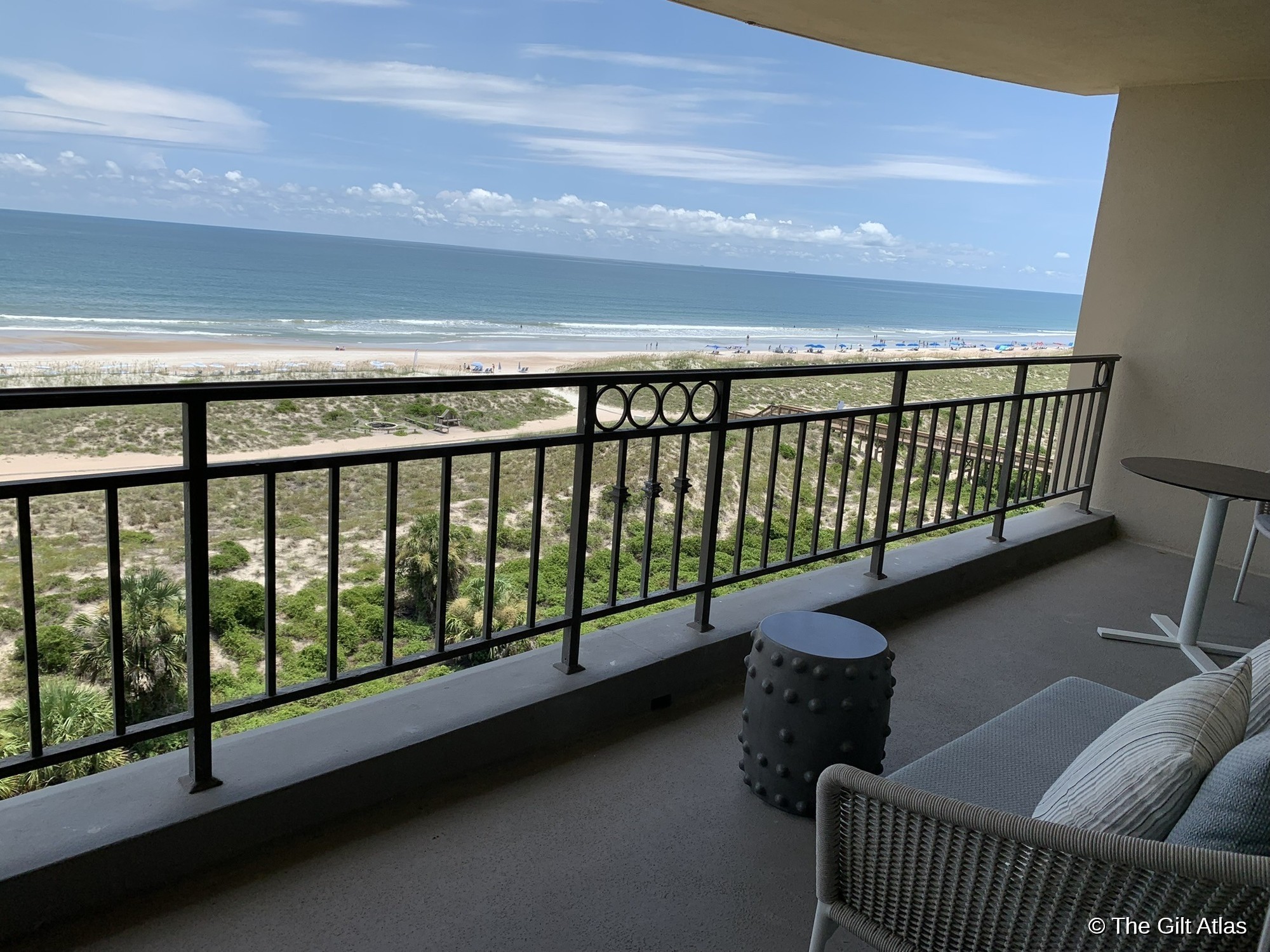 Corner suite balcony at Ritz-Carlton Amelia Island — wicker sofa, circular railing detail, ocean and beach visible beyond the dunes