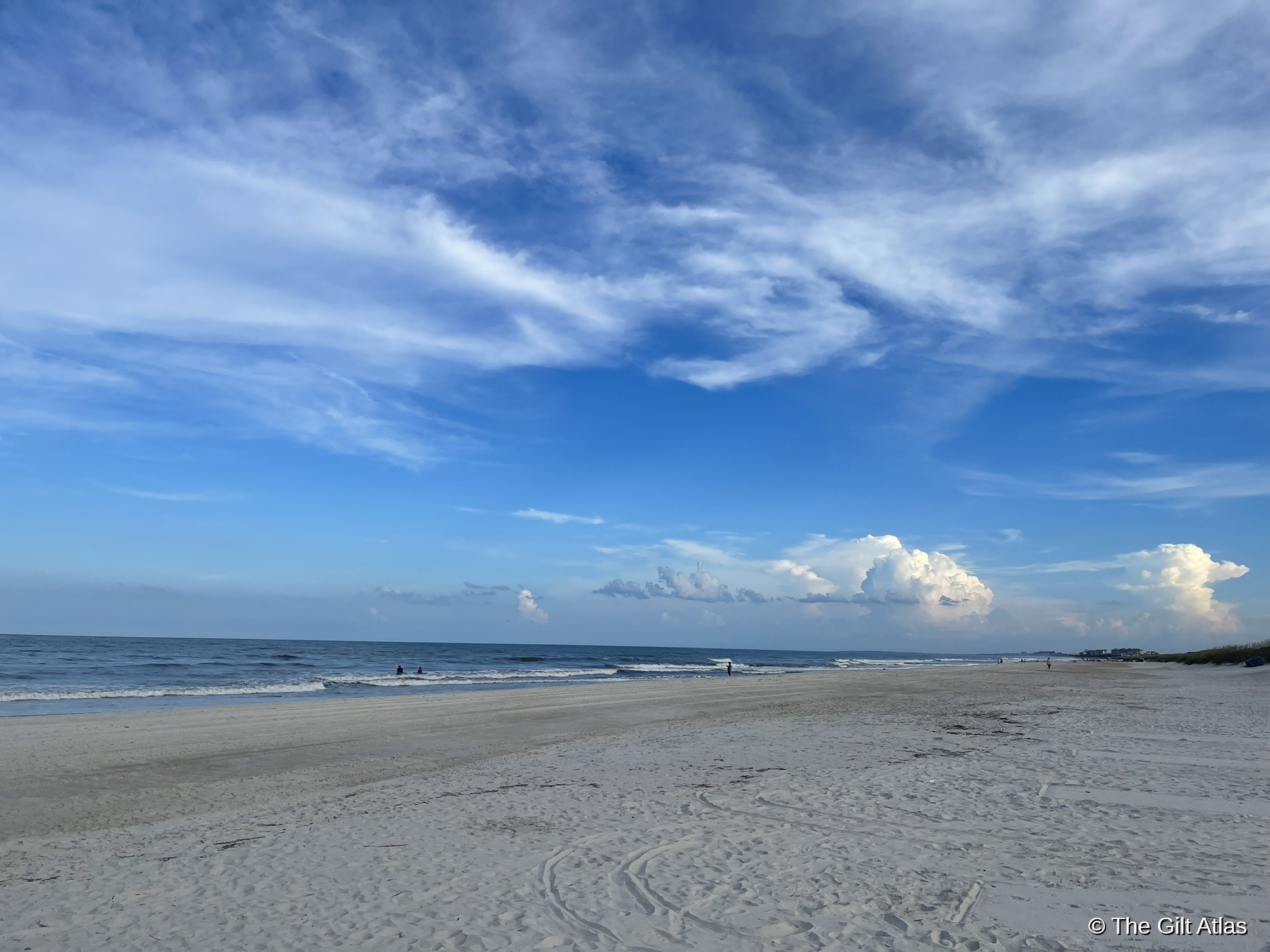 Amelia Island beach — wide pale sand, a handful of people in the distance, dramatic cumulus clouds building on the horizon over the Atlantic