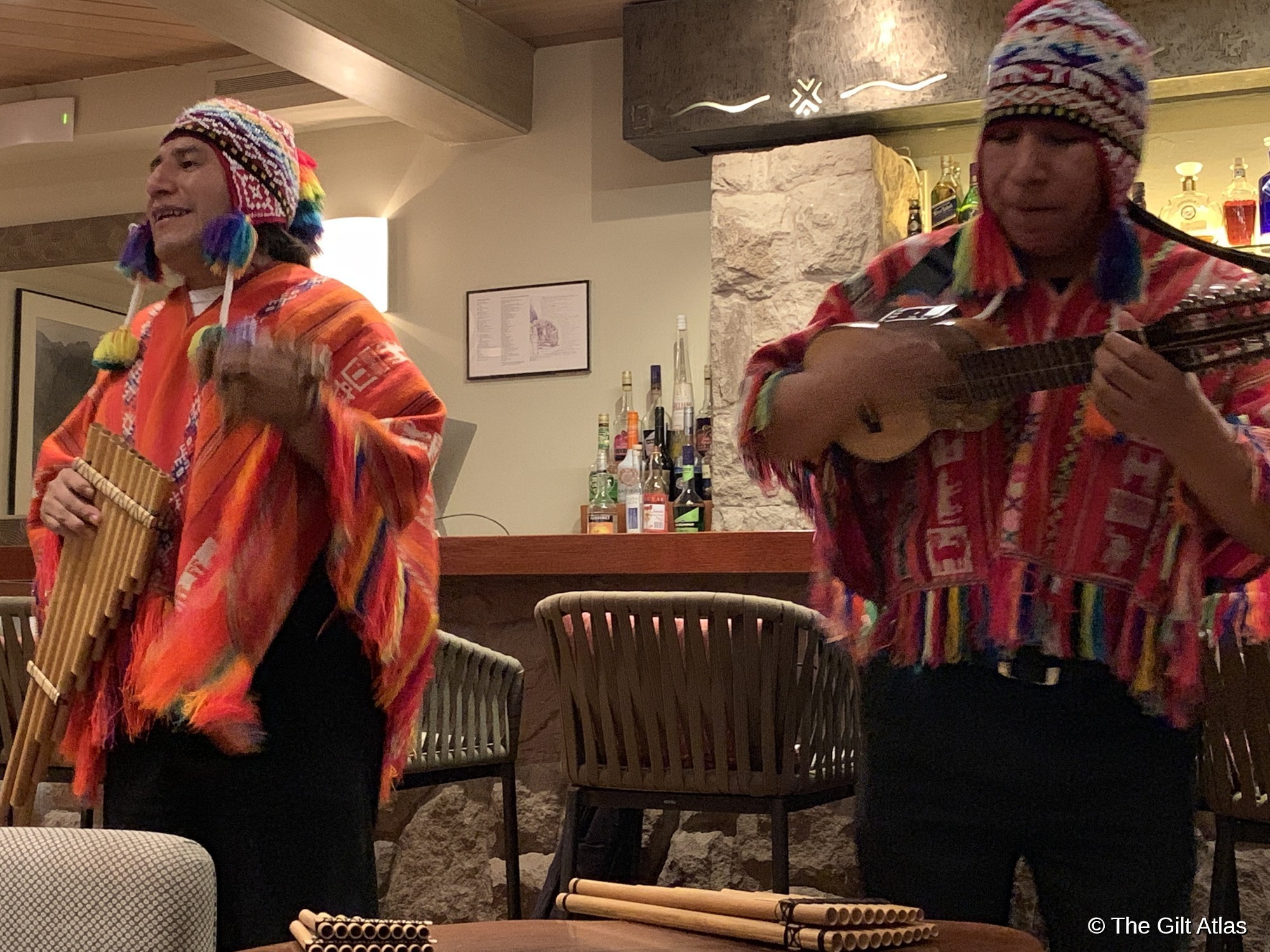 Two musicians in traditional colorful Andean dress performing with pan flutes and a charango in the lodge's dining room