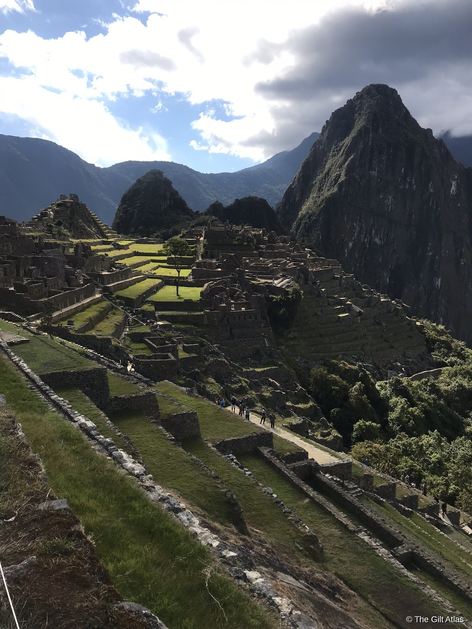 Machu Picchu citadel and Huayna Picchu peak seen from above, with sun breaking through clouds