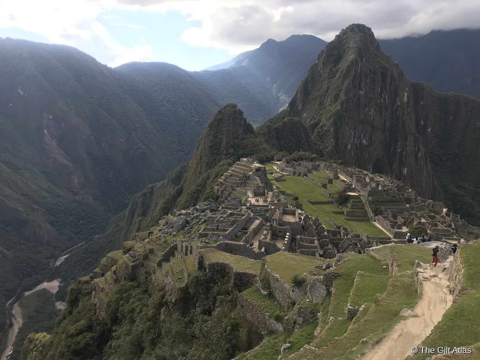 Wide panoramic view of Machu Picchu terraces and surrounding peaks under a dramatic cloudy sky