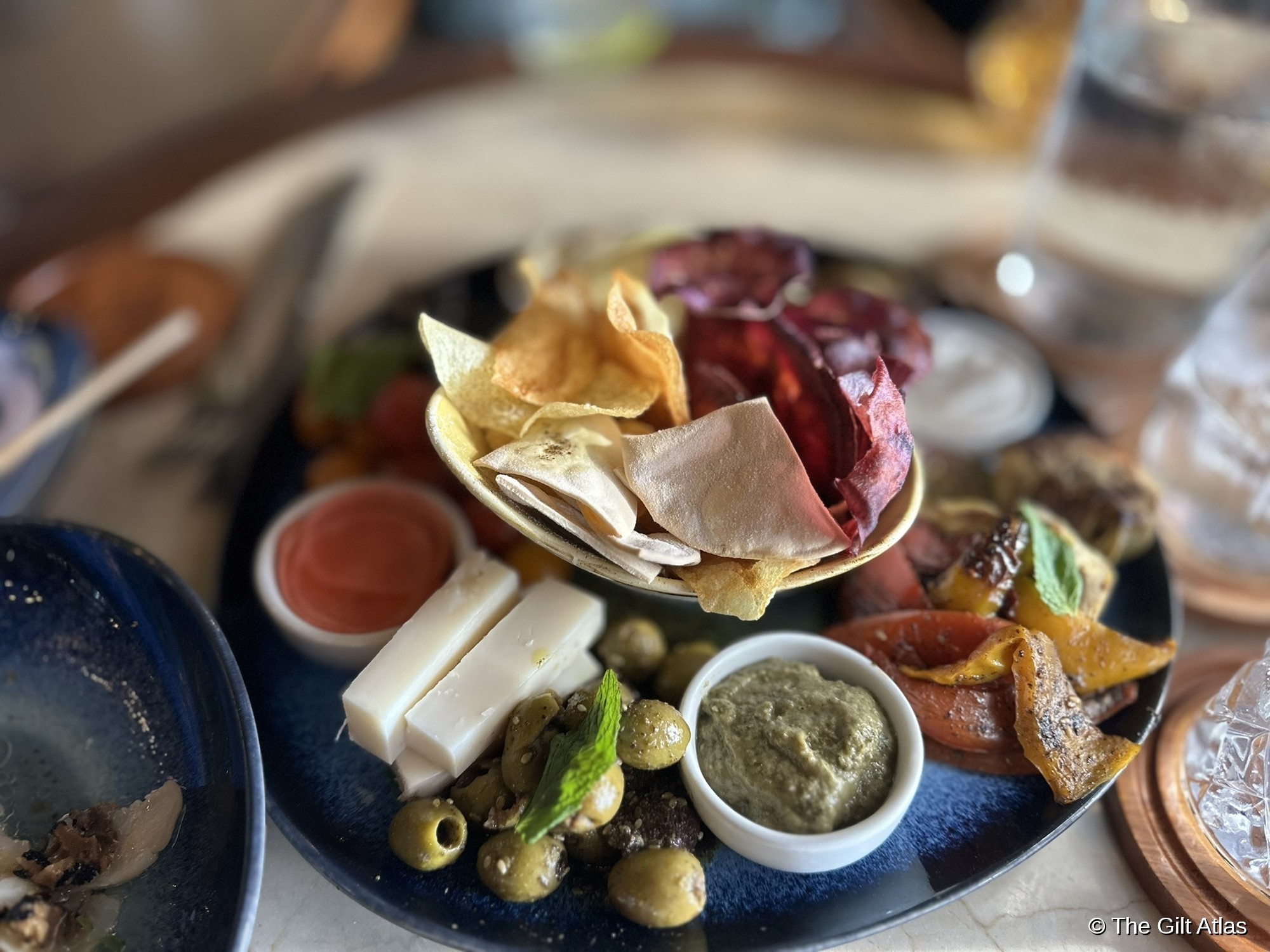 Restaurant appetizer plate at Hotel das Cataratas — charcuterie, chips, olives, cheese, dips and roasted vegetables on a blue ceramic plate