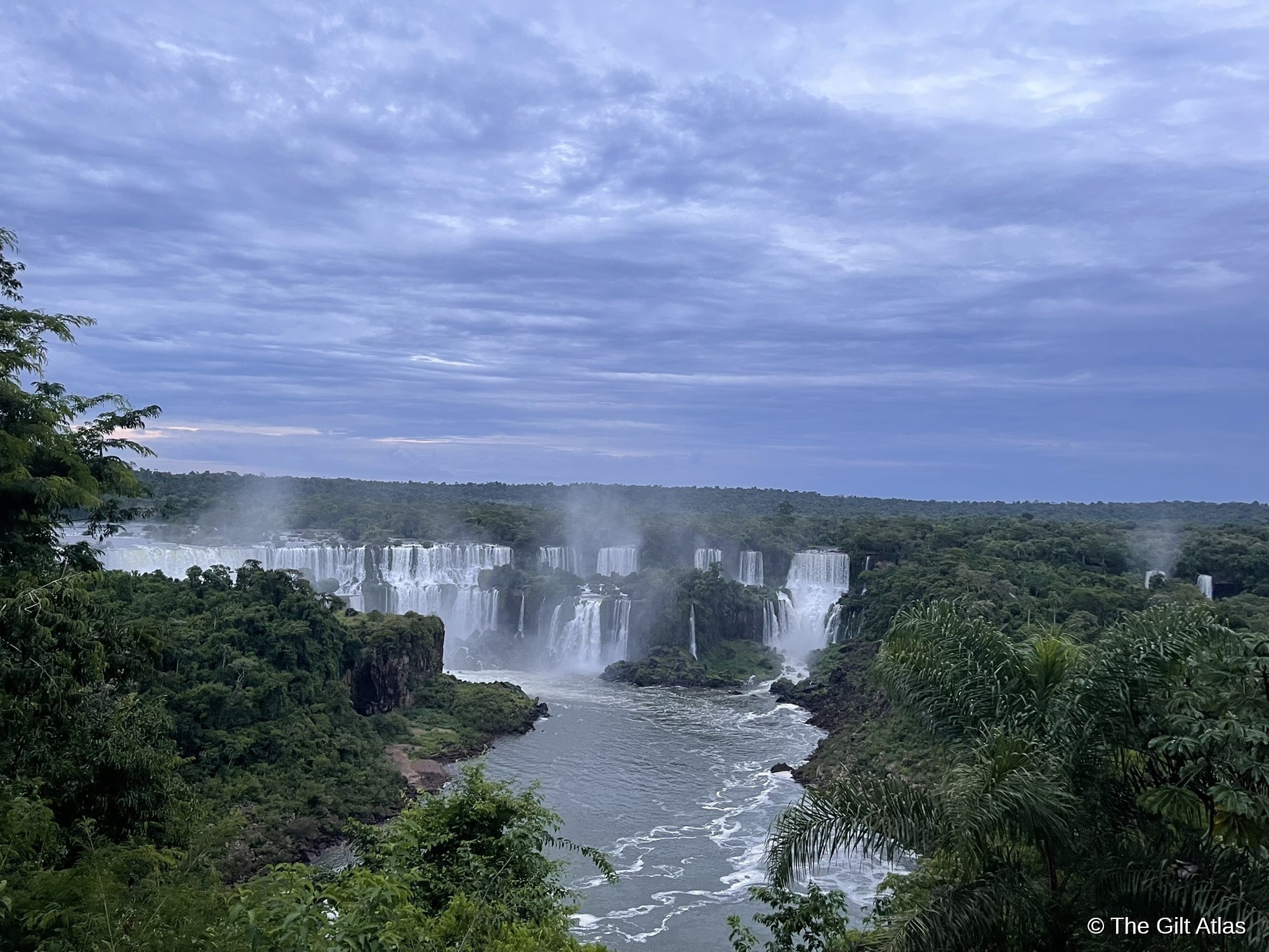 Iguazu Falls at early morning — blue pre-dawn light, mist rising from the falls, no crowds on the boardwalks