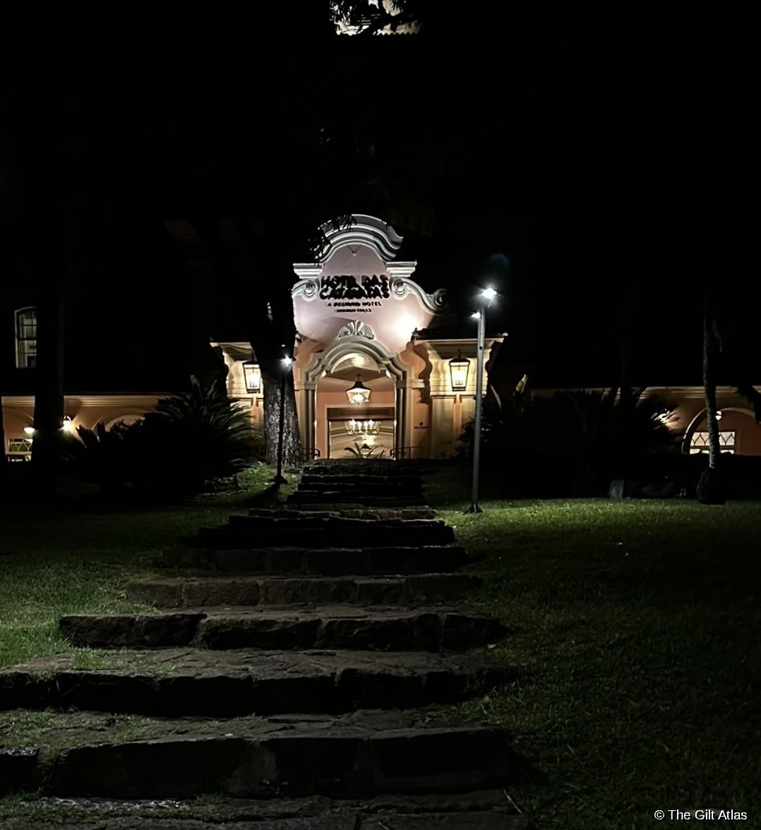 Hotel das Cataratas entrance at night — pink colonial facade illuminated, stone steps, lanterns, Belmond signage