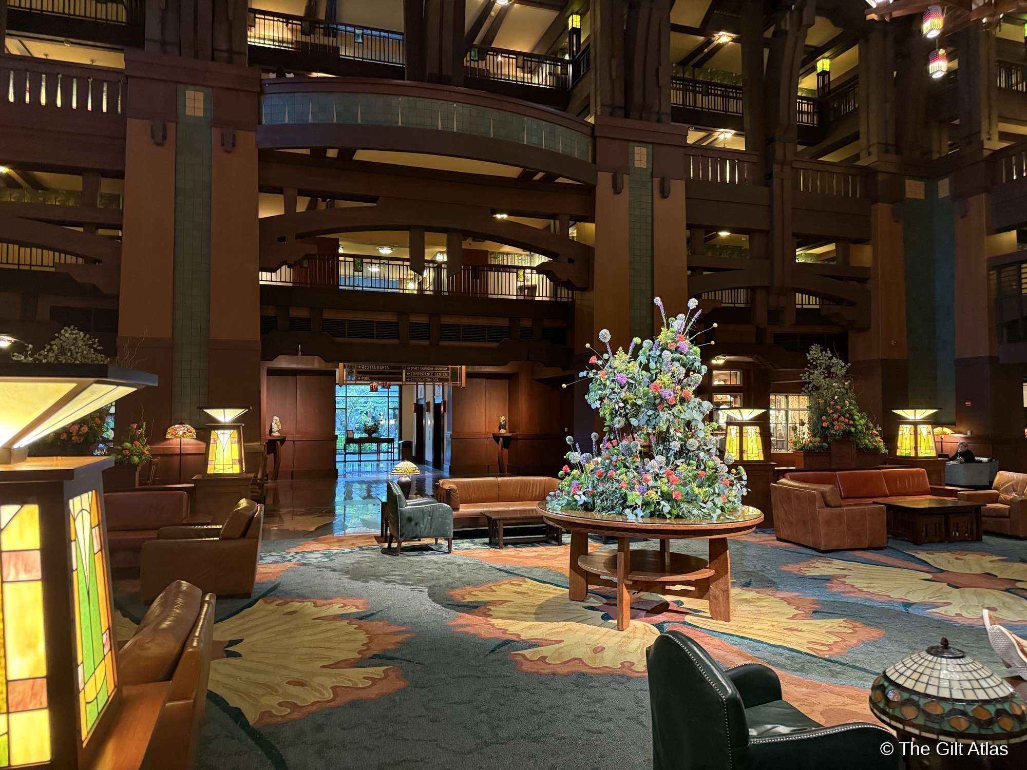The Grand Lobby of Disney's Grand Californian Hotel & Spa &mdash; a six-story Arts and Crafts atrium with a central floral arrangement, stained glass lamps, Arts and Crafts carpet, and timber balconies rising above