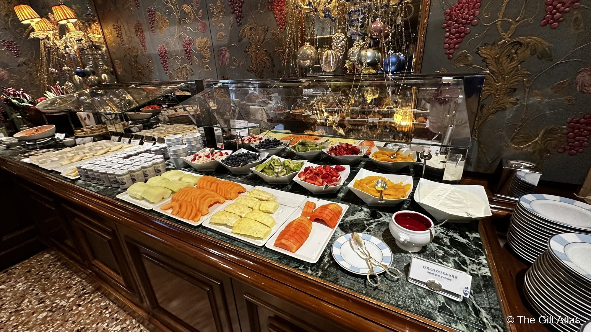 The Club del Doge breakfast buffet at the Gritti Palace — fresh fruit, smoked salmon, and pastries on a marble counter beneath ornate Venetian decor