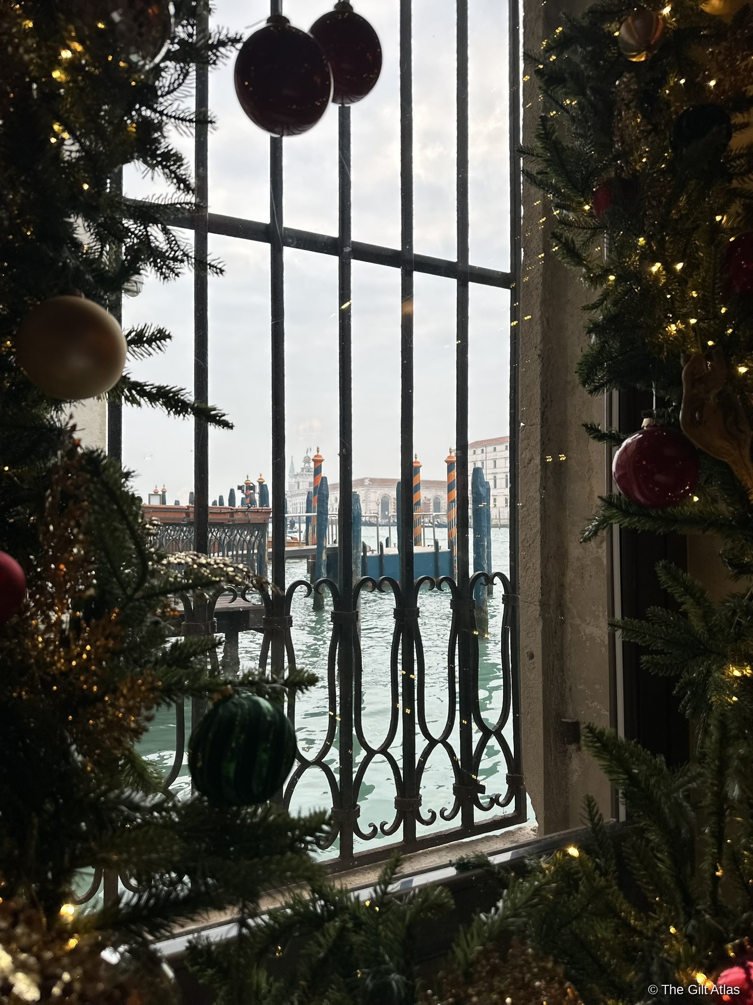 The Grand Canal through an ornate iron window at the Gritti Palace, framed by Christmas trees on New Year's Eve