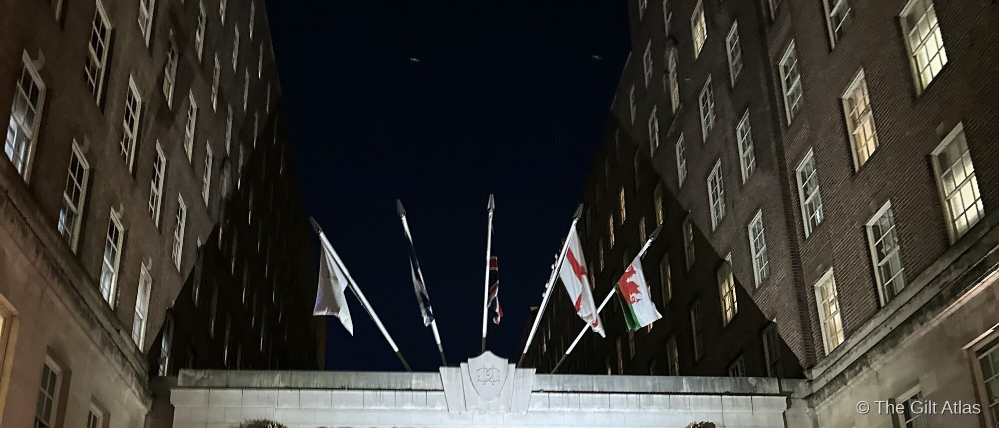 The Grosvenor House entrance on Park Lane at night, lit with Christmas decorations, wreaths, and festive trees — flags of England and Wales flying above the illuminated canopy