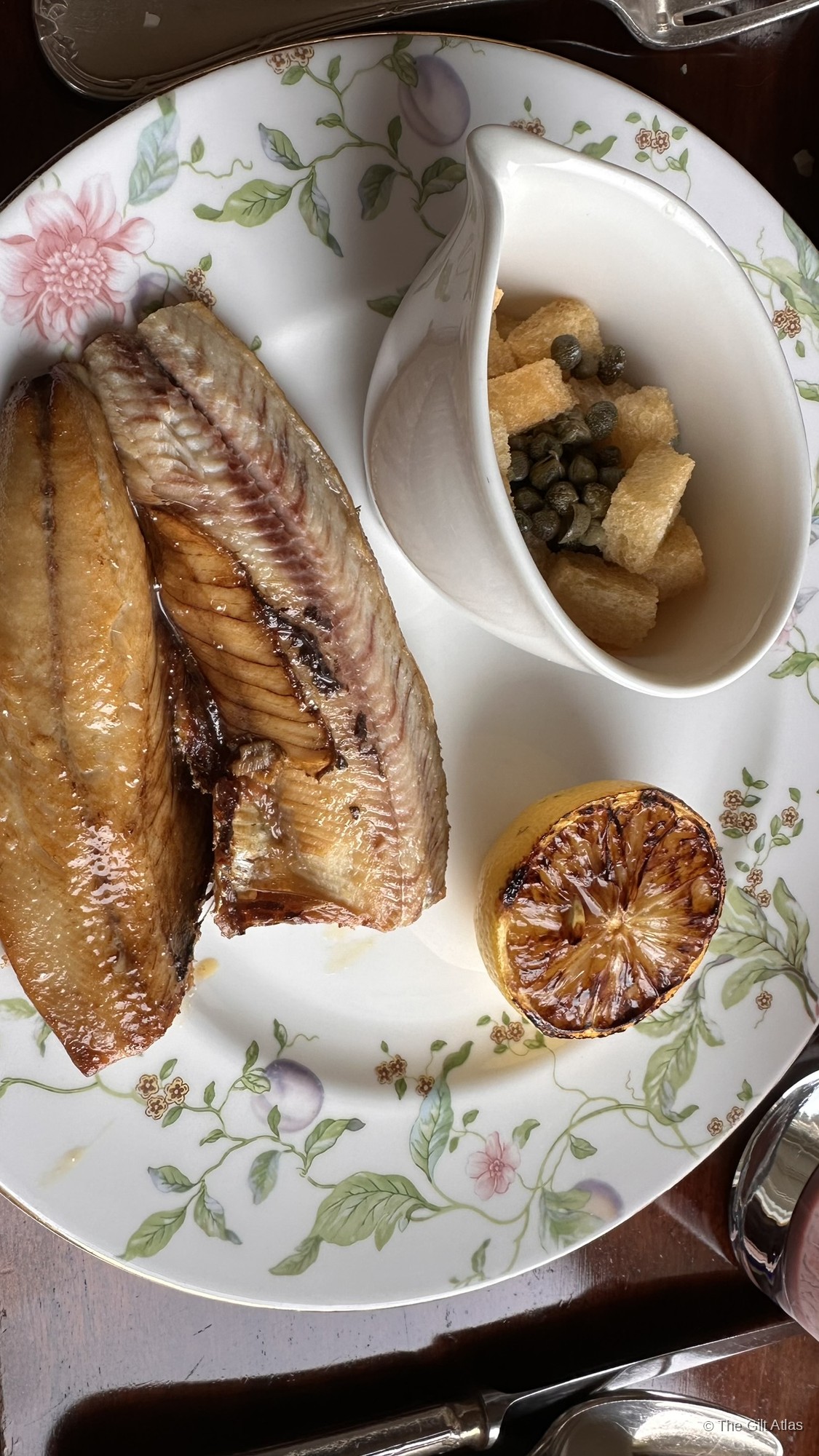 Smoked kipper on Inverlochy Castle's floral-bordered china, served with capers, croutons, and a charred lemon half.
