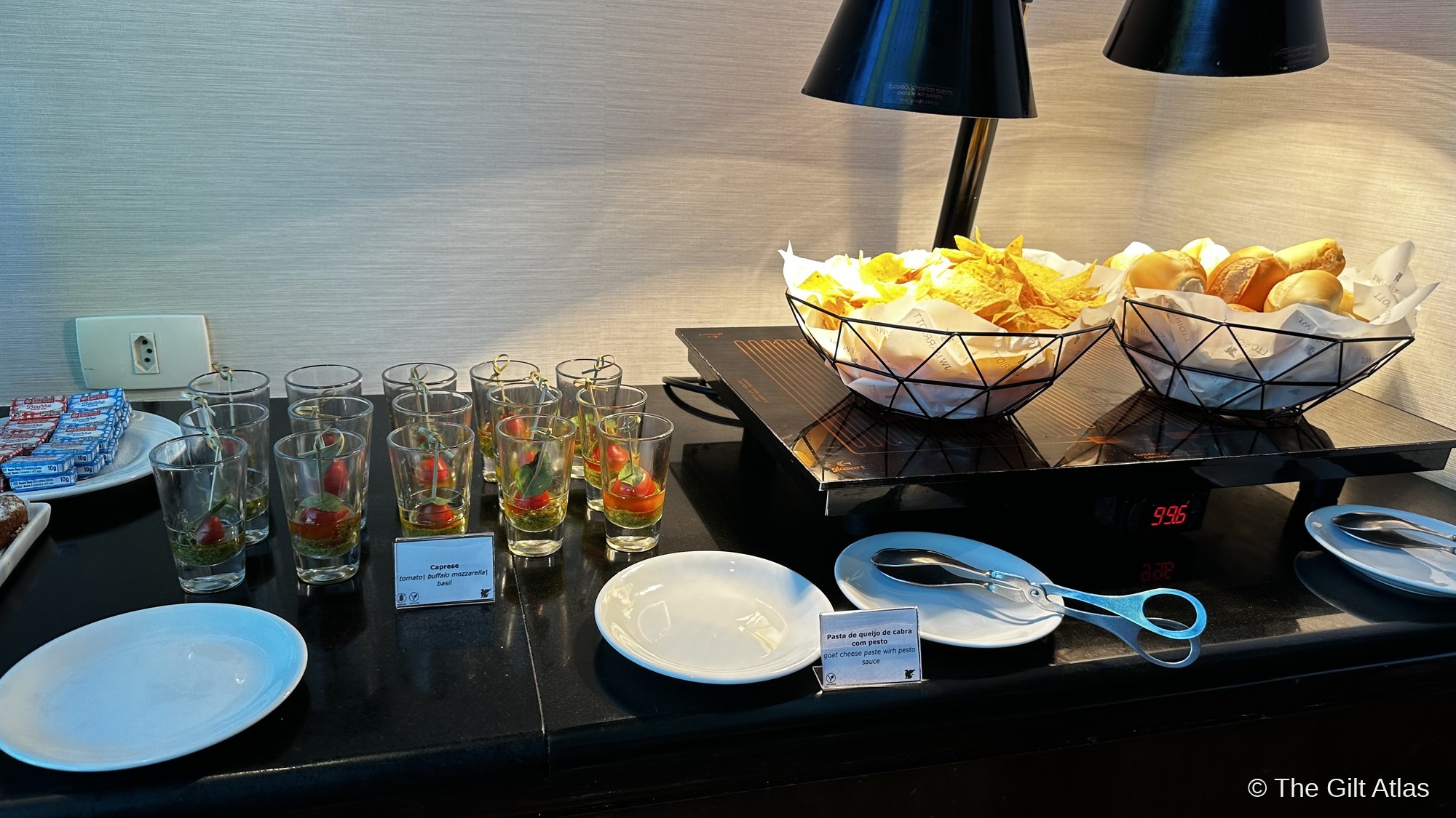 JW Marriott Rio executive lounge evening appetizer spread — caprese salad in shot glasses, goat cheese paste with pesto, breads and chips in wire baskets, bilingual label cards
