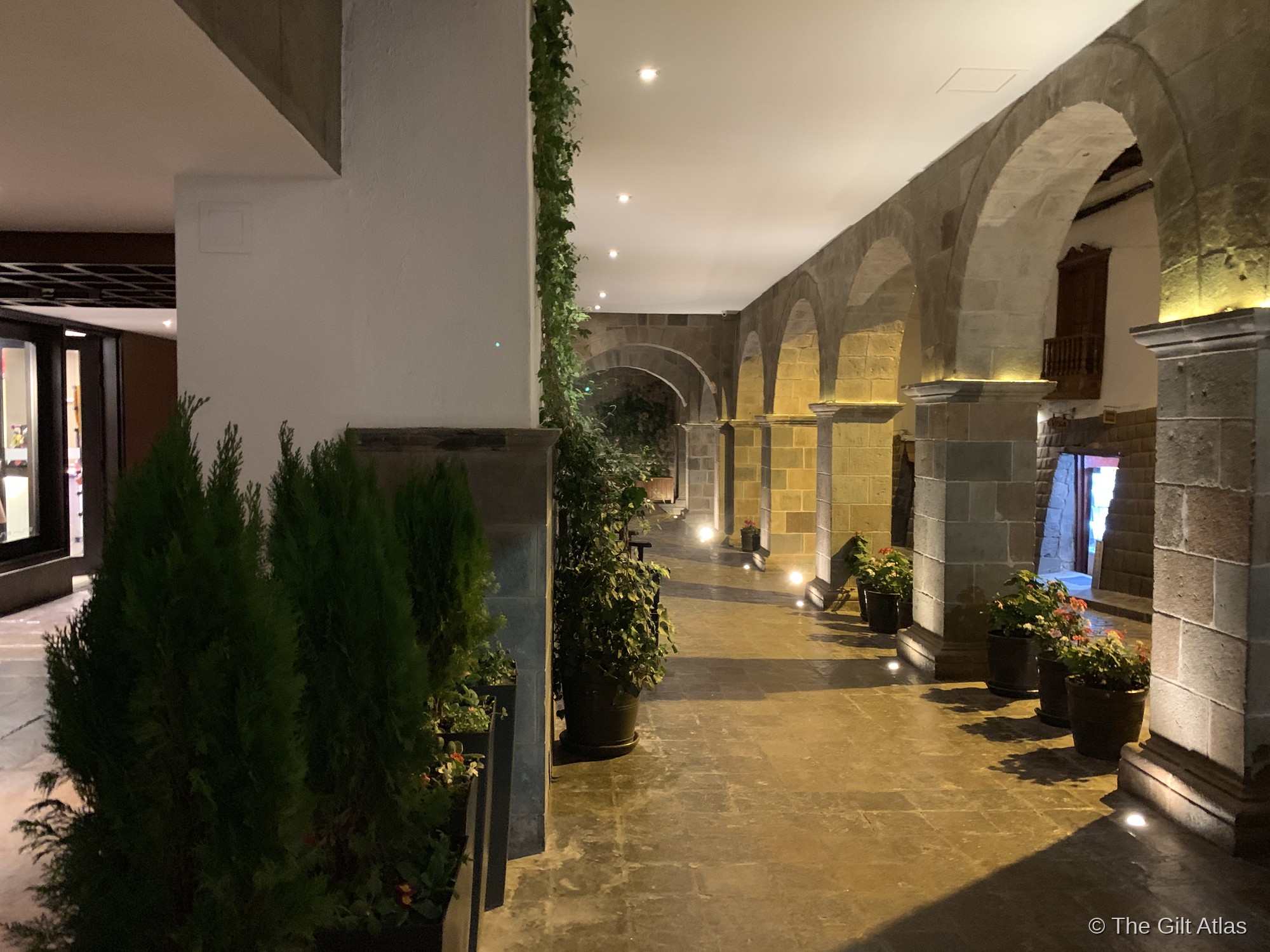 The Palacio del Inka's colonial arched courtyard, lit at night, with stone columns, potted plants, and warm lighting