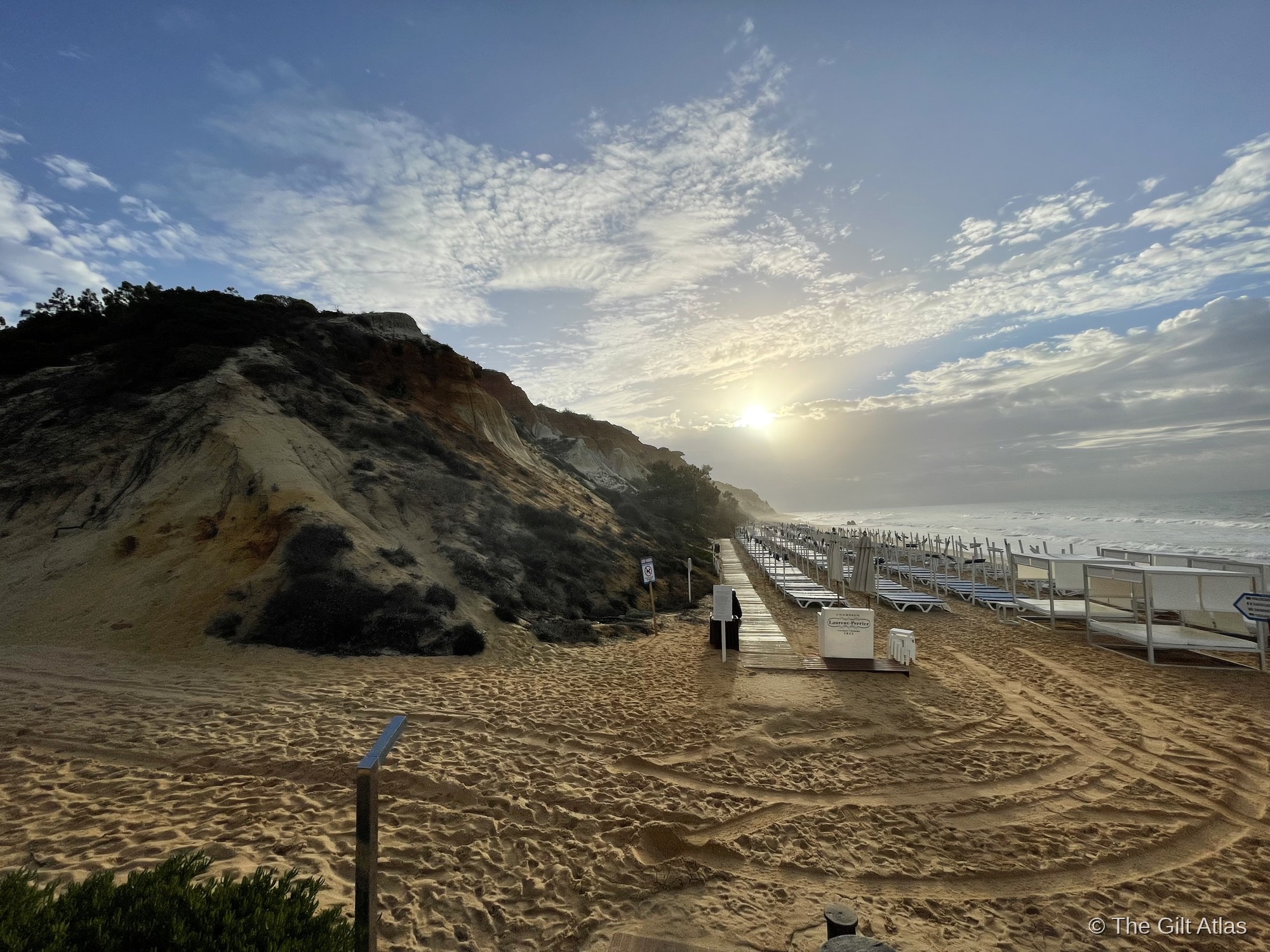 The ochre sandstone cliffs of Praia da Falésia at dawn, with beach chairs stretching along the sand and dramatic clouds above