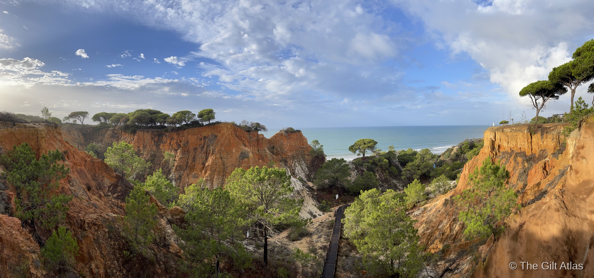 Panoramic view of the sandstone ravine at Pine Cliffs with the boardwalk path winding through ochre cliffs to the Atlantic beyond