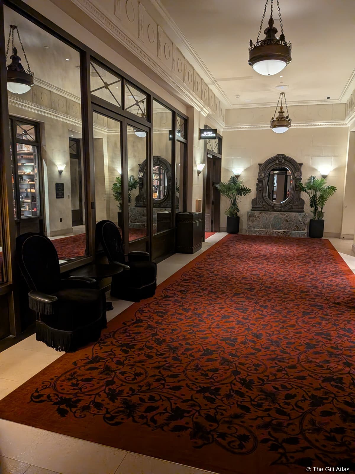 The Reserve Las Vegas — quiet corridor leading directly to the guest elevators, deep red patterned carpet, ornate antique mirror on pedestal, palm fronds, no crowds