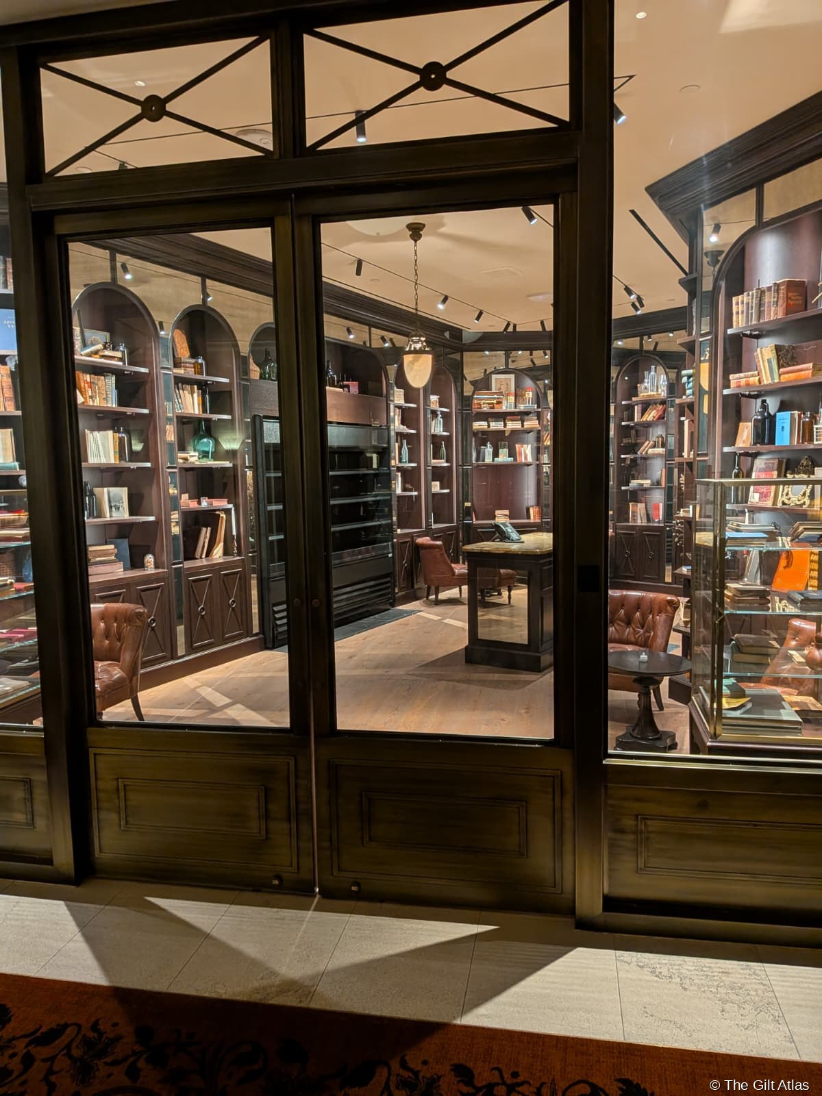 The Reserve Las Vegas library — dark walnut arched bookshelves floor to ceiling seen through glass-paned doors, leather Chesterfield armchairs, pendant lantern lighting, parquet oak floor