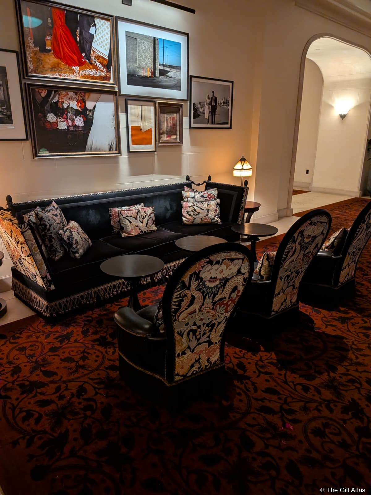The Reserve Las Vegas lobby seating area — black velvet sofa with floral cushions, bold gallery wall of framed contemporary photographs, patterned carpet in deep red and burnt orange
