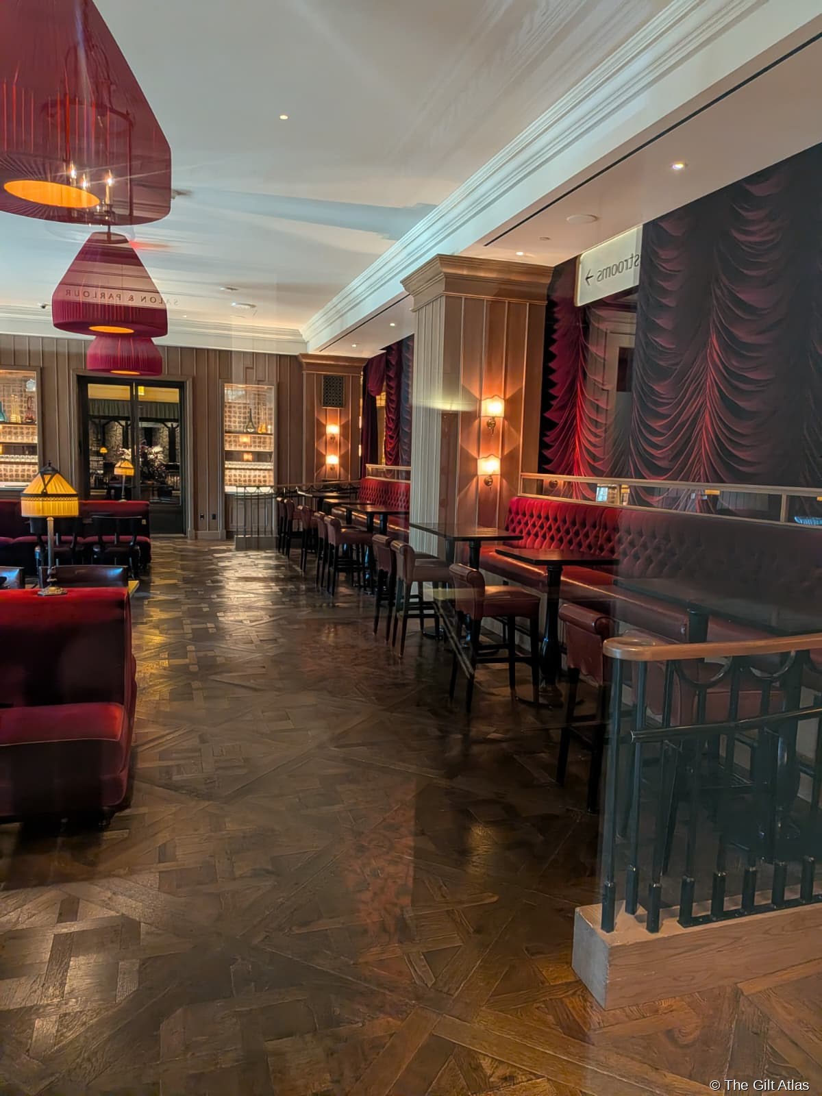 Salon & Parlour at The Reserve Las Vegas — crimson velvet banquettes and parquet herringbone floor, dramatic pendant lamps in deep red, bar visible at the far end, empty in the afternoon before service