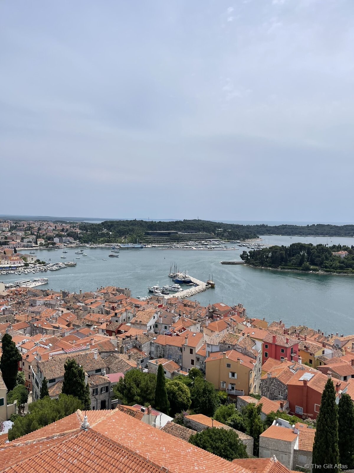 Aerial panorama of Rovinj from the St. Euphemia campanile, showing orange rooftops, the harbour, and the Adriatic islands beyond