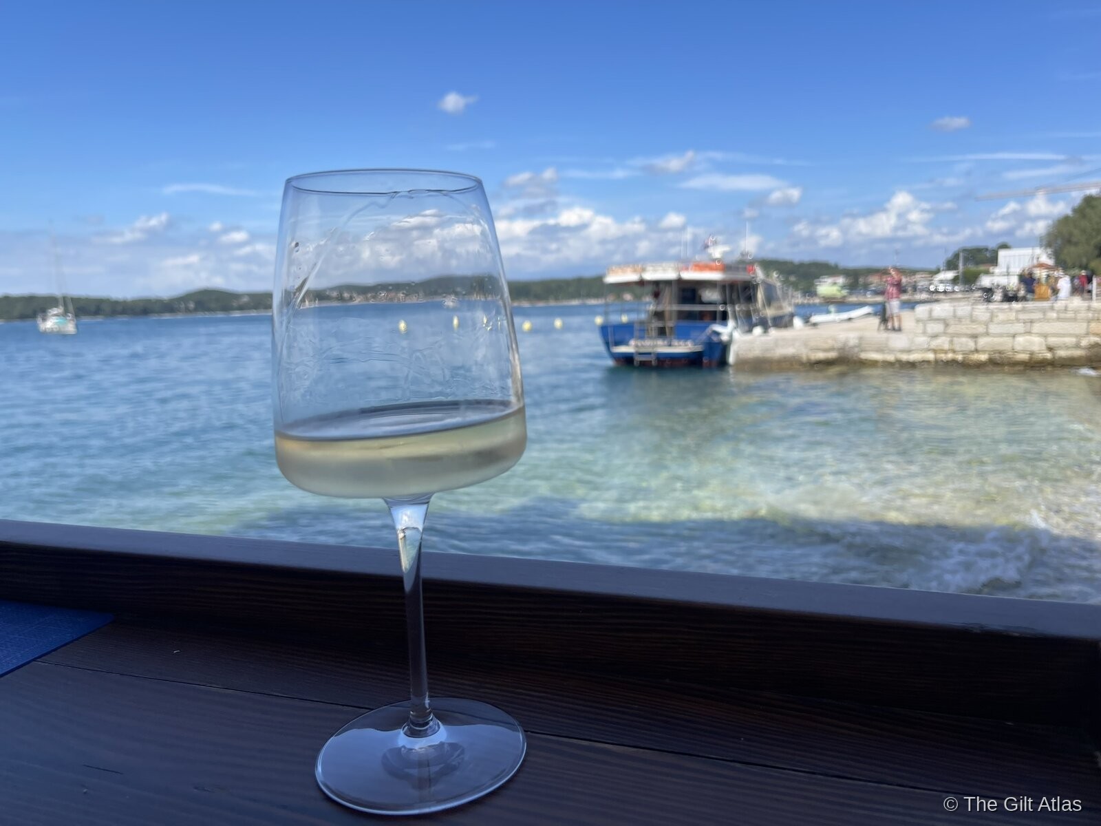 A glass of Istrian white wine at the hotel waterfront lounge, with boats and the harbour visible beyond