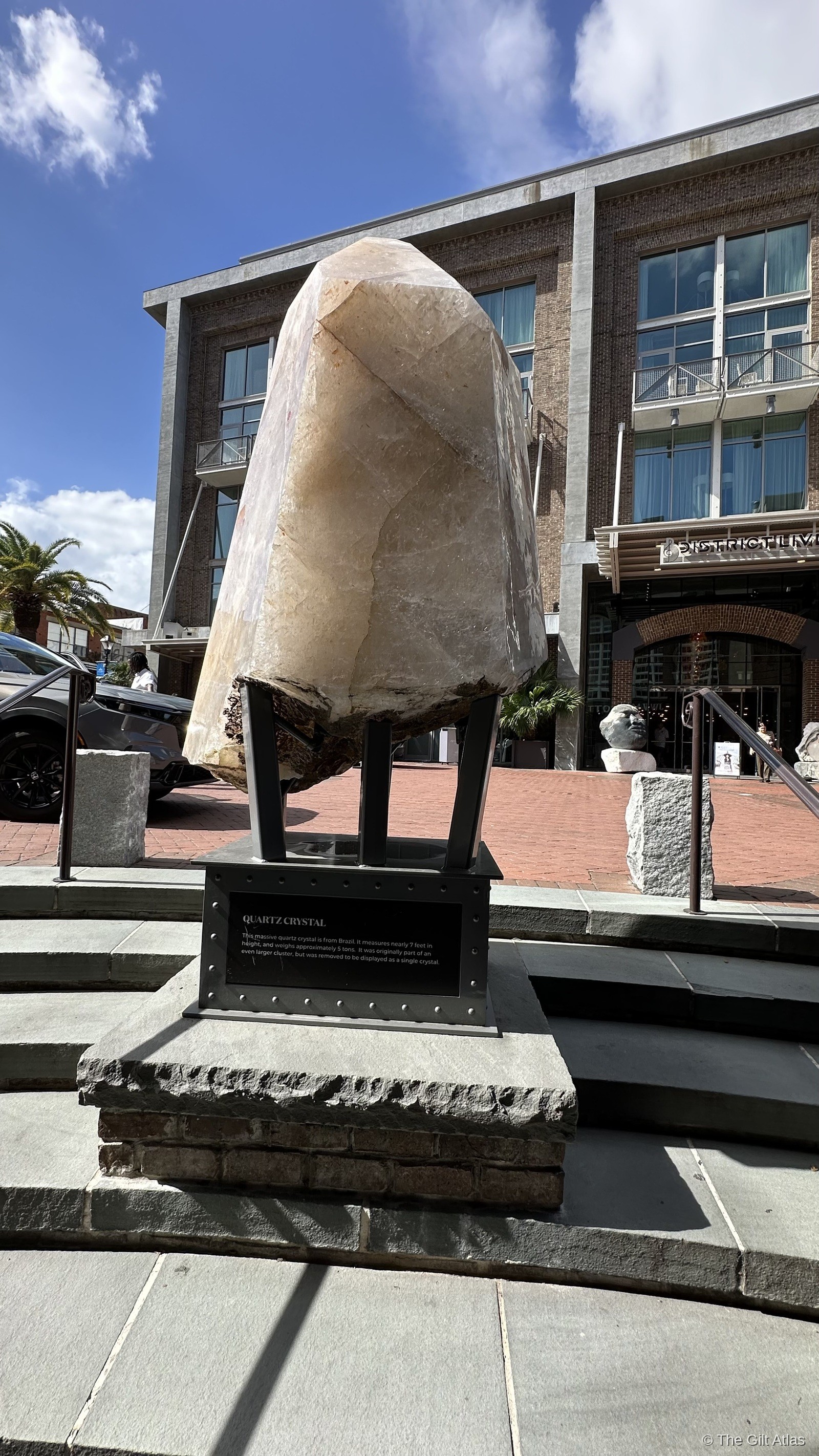 A massive quartz crystal on a steel display plinth outside the Plant Riverside District entrance, with the brick hotel building visible behind it