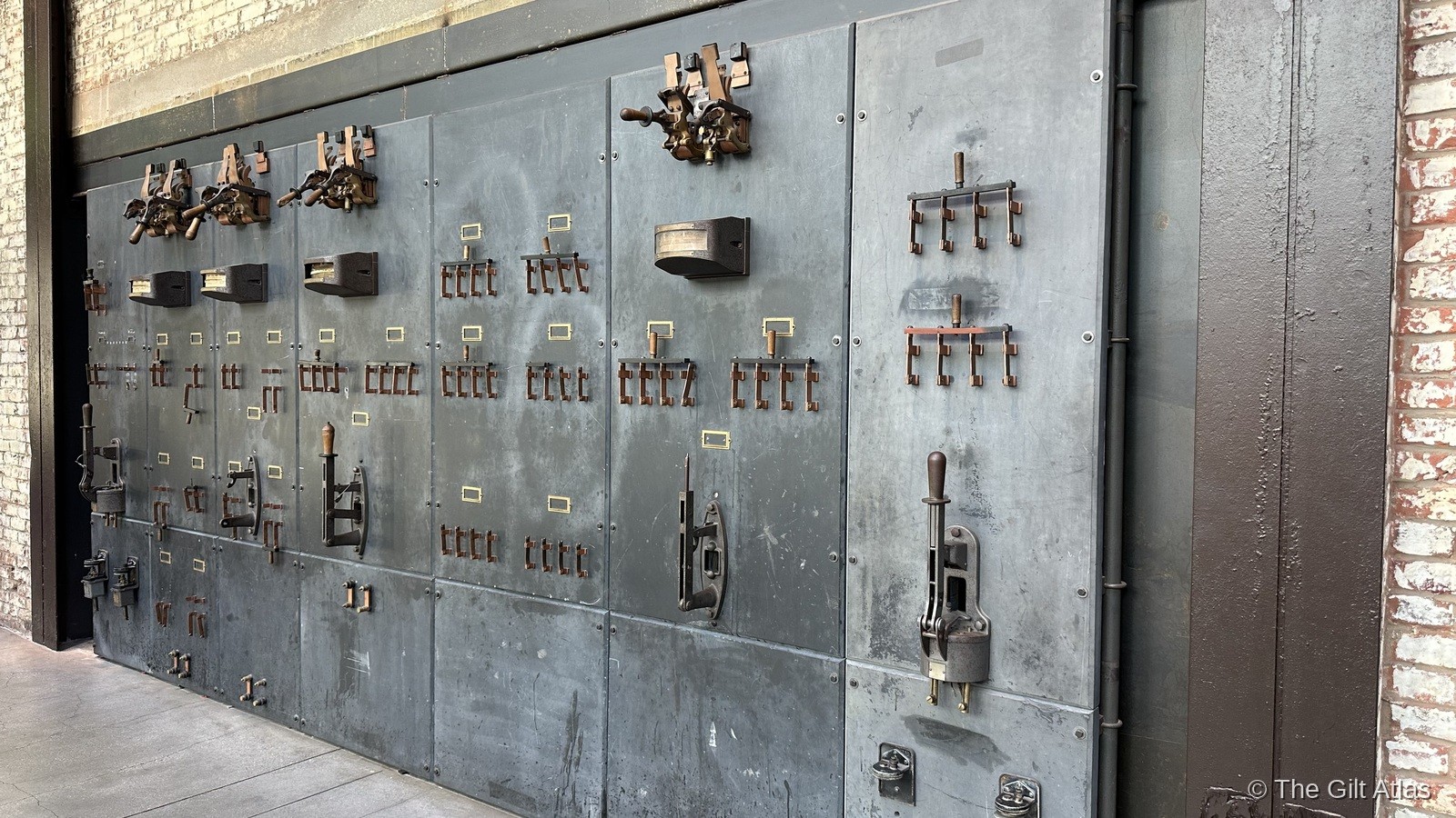 A restored antique electrical switchboard mounted on the brick wall — the original industrial control panels from the 1912 power plant, preserved as part of the building's heritage display