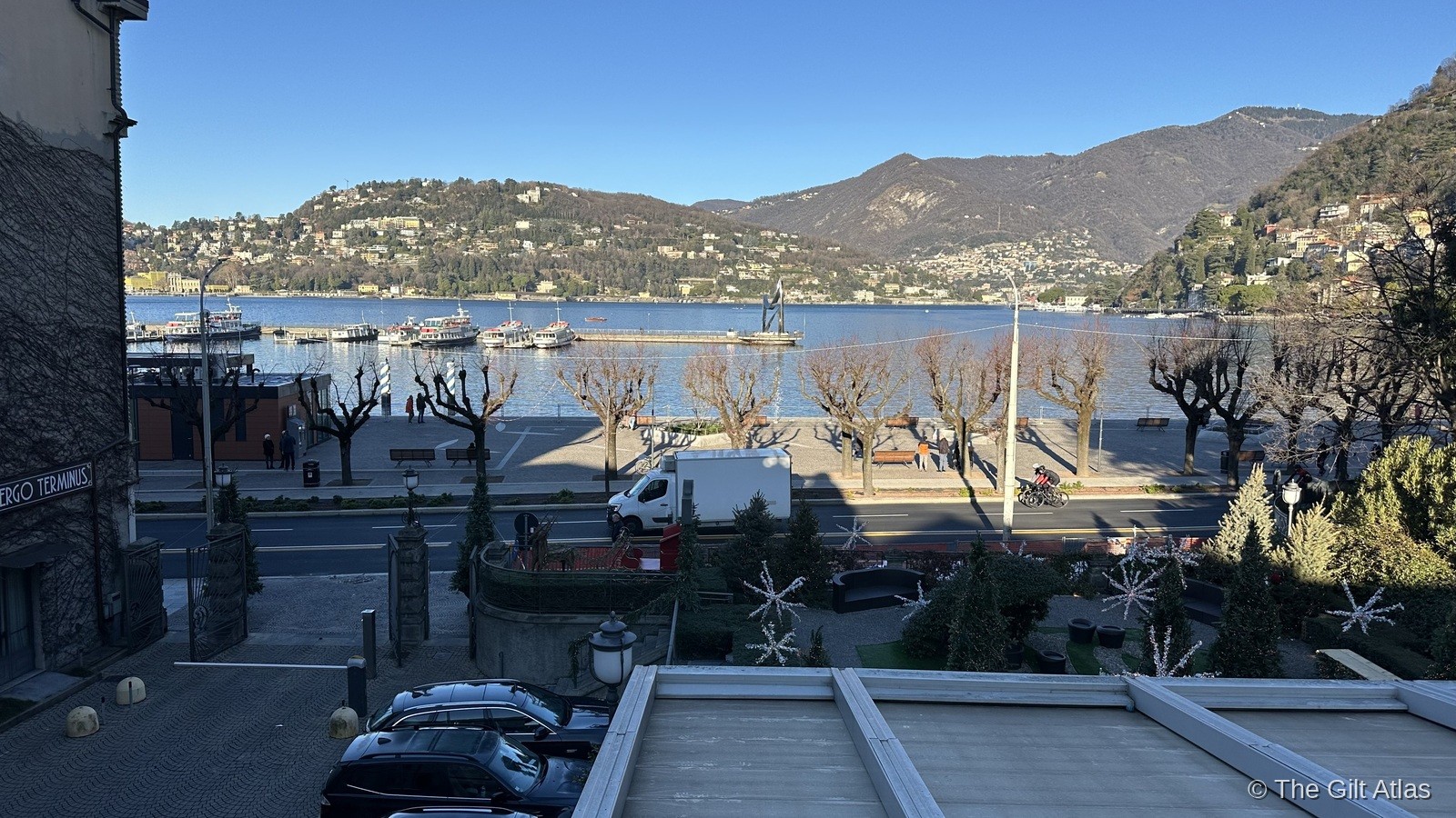 Lake Como from the Hotel Terminus terrace — the ferry pier, promenade, and Alps beyond on a clear January morning