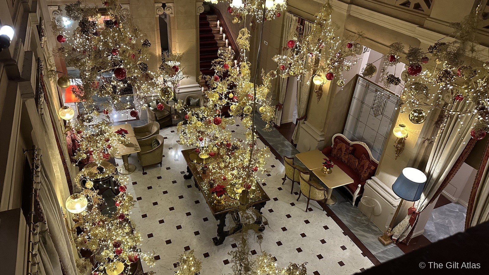 Hotel Terminus Lake Como lobby from above — Christmas trees, fairy lights, and ornate marble floors viewed from the upper landing