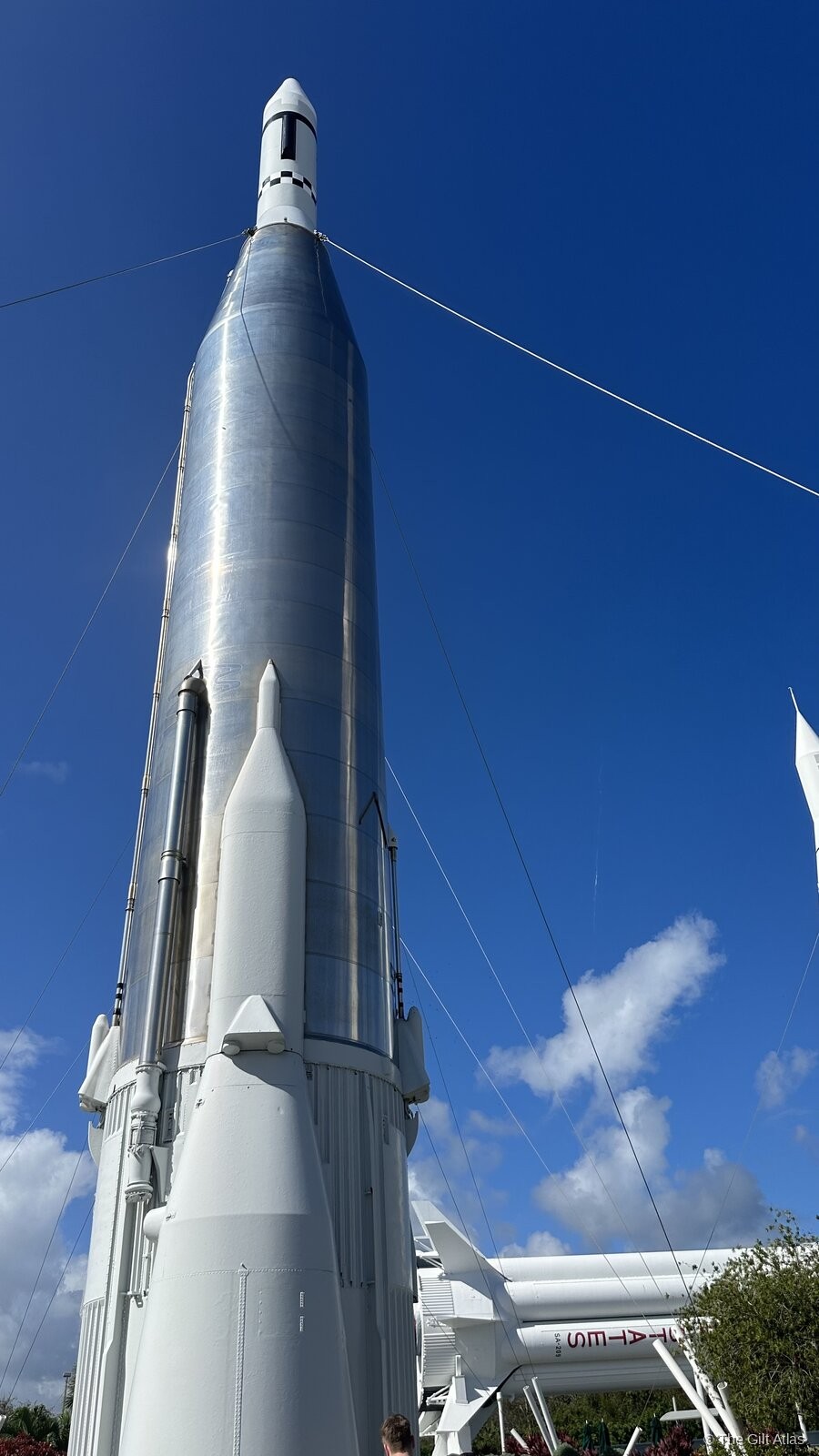 A Saturn-era rocket in the Kennedy Space Center Rocket Garden — stainless steel body with white boosters rising against a deep blue Florida sky