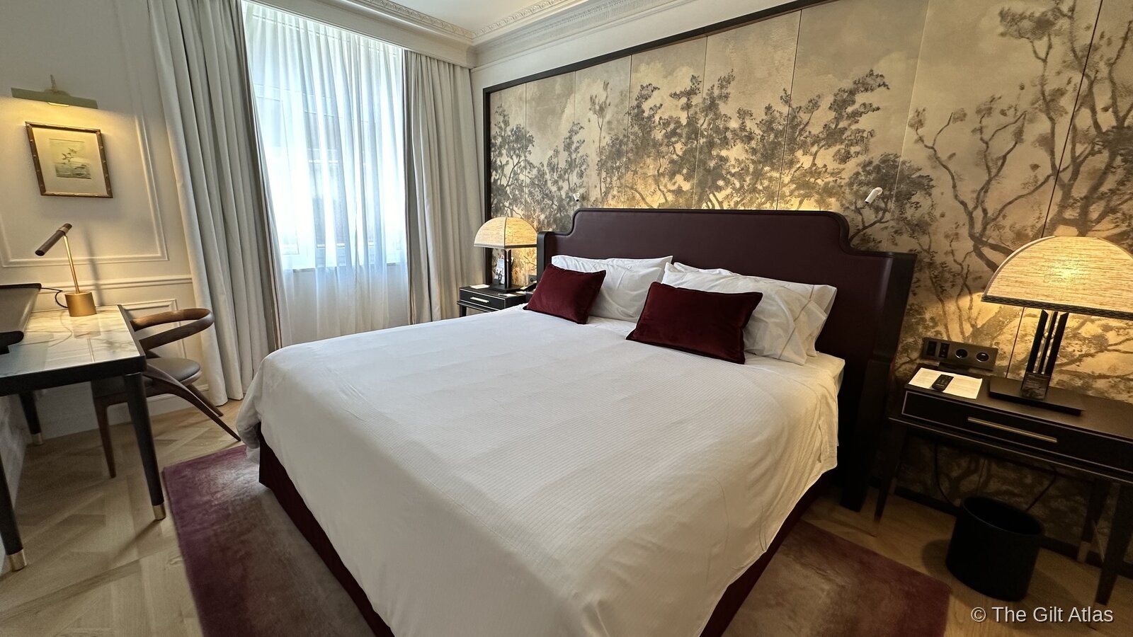 The suite bedroom — king bed with burgundy velvet pillows against a dramatic hand-painted mural of trees on the headboard wall, warm bedside lamps, parquet floors