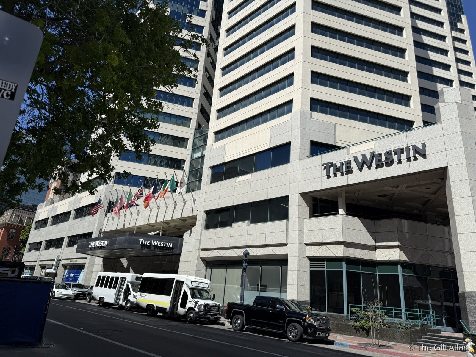 The Westin San Diego Bayview exterior — stone facade with stepped crown, Westin signage, flags lining the entrance canopy, hotel shuttle at the curb