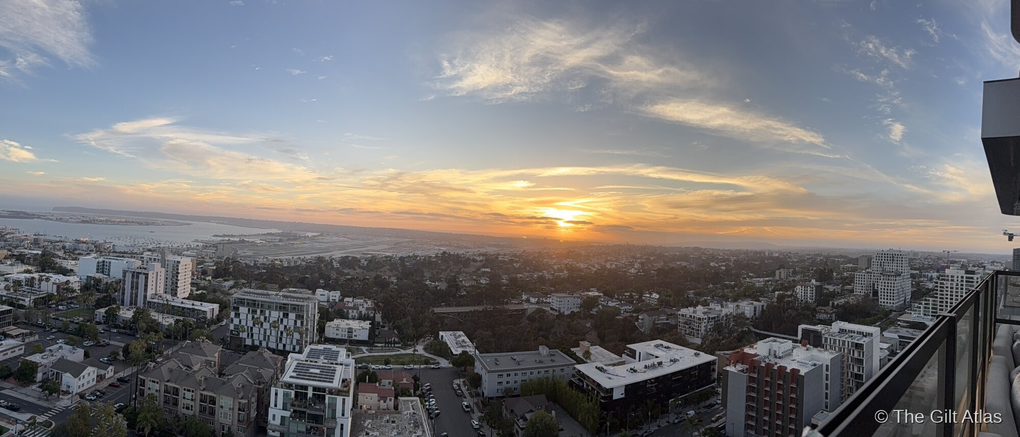 Panoramic sunset over San Diego — the city spreading west toward the bay and airport, golden light across the horizon, viewed from downtown